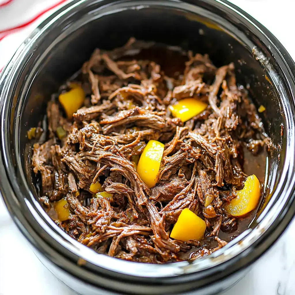 A close-up view of shredded beef cooked in a slow cooker, mixed with small pieces of yellow peppers.