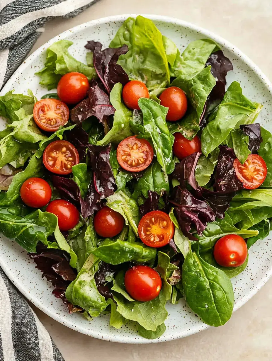 A vibrant salad featuring a mix of leafy greens and halved cherry tomatoes served in a speckled white bowl.