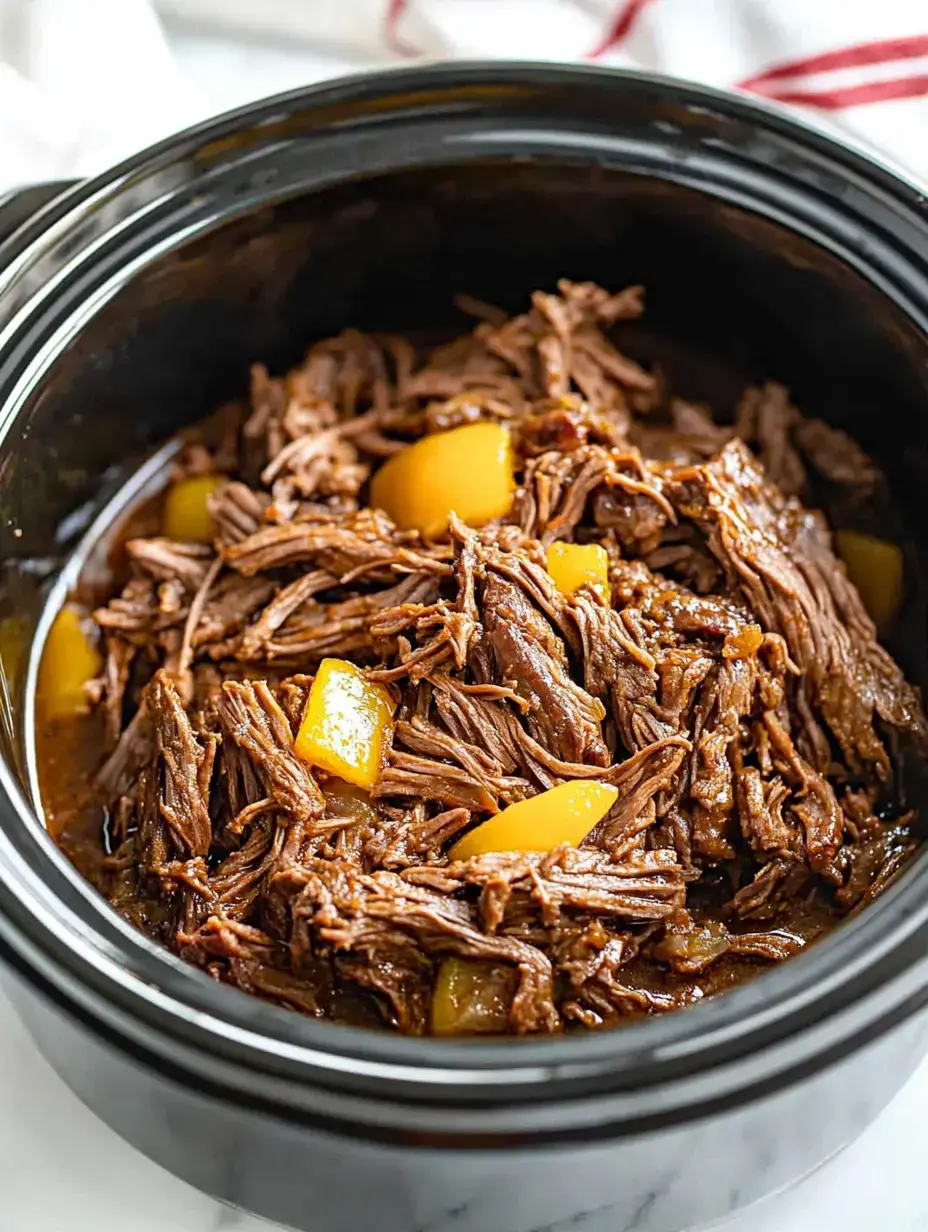 A close-up of shredded beef cooked with yellow vegetables in a black slow cooker.