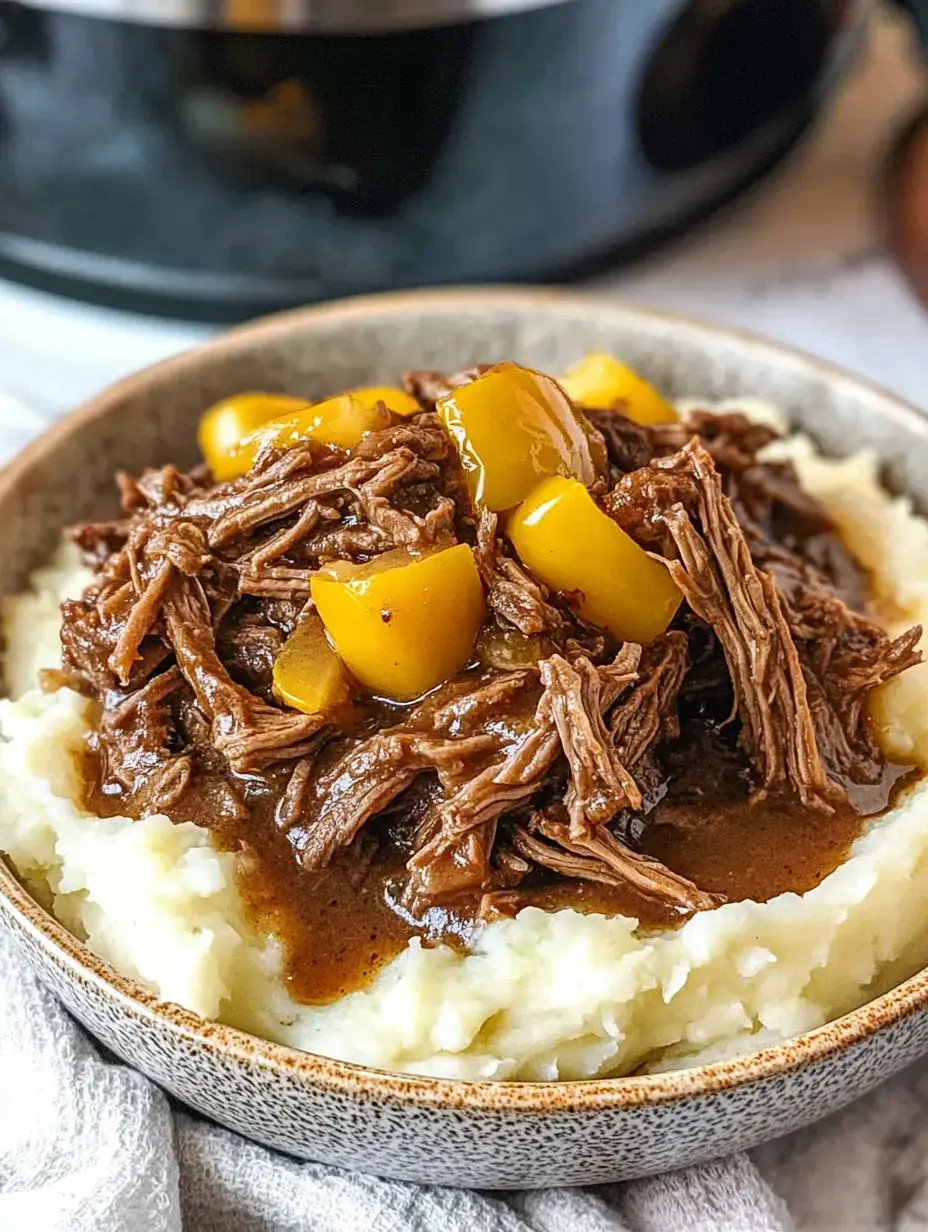 A bowl of mashed potatoes topped with shredded beef and yellow peppers in a gravy sauce.