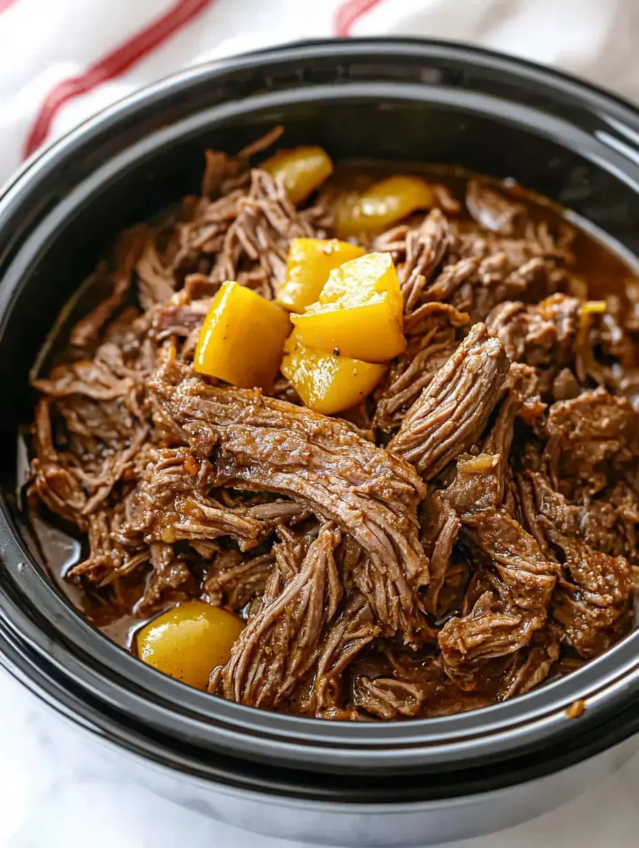 A close-up of shredded beef cooked in a slow cooker, topped with pieces of yellow fruit.