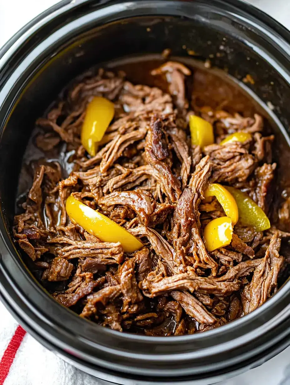 A close-up of shredded beef cooked in a slow cooker, garnished with yellow bell pepper slices in a savory sauce.