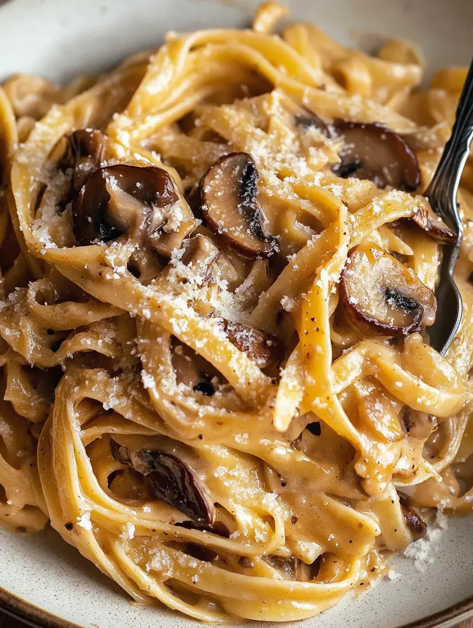 A close-up of a plate of fettuccine pasta topped with mushrooms and sprinkled with grated cheese.