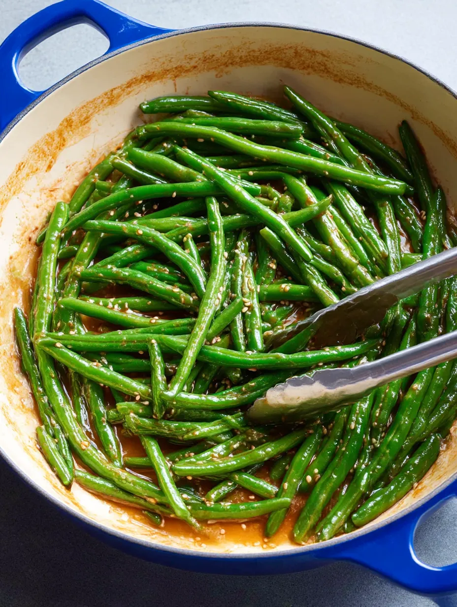 A pan of green beans with a spoon in it.