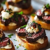 A close-up of toasted bread topped with slices of steak, creamy sauce, and garnished with chopped herbs.