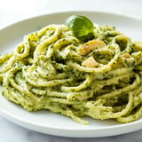 A plate of spaghetti tossed in green pesto sauce, garnished with a fresh basil leaf.