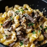 A close-up of creamy pasta mixed with beef chunks and garnished with parsley.