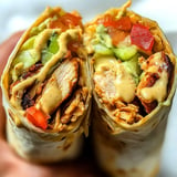 A close-up of a halved burrito filled with grilled chicken, lettuce, diced tomatoes, and a creamy sauce.