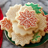 A decorative assortment of snowflake-shaped cookies, featuring intricate icing designs in various colors, stacked on a green plate.