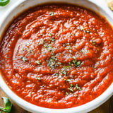 A bowl of rich red tomato sauce is garnished with herbs and spices.