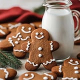 A plate of decorated gingerbread cookies is displayed alongside a pitcher of milk, set against a festive background.