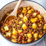 A pot filled with cooked ground meat and yellow potatoes, garnished with herbs and mixed with diced vegetables.