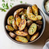 A bowl of crispy roasted potatoes garnished with herbs and sprinkled with salt.