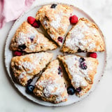 A plate of freshly baked scones topped with powdered sugar and garnished with raspberries and blueberries.