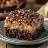 A slice of layered chocolate cake topped with a glossy chocolate ganache and sprinkled with chocolate chips on a blue plate.