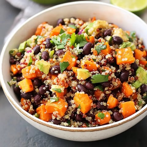 A colorful bowl of quinoa salad mixed with black beans, diced sweet potatoes, avocado, and fresh cilantro.